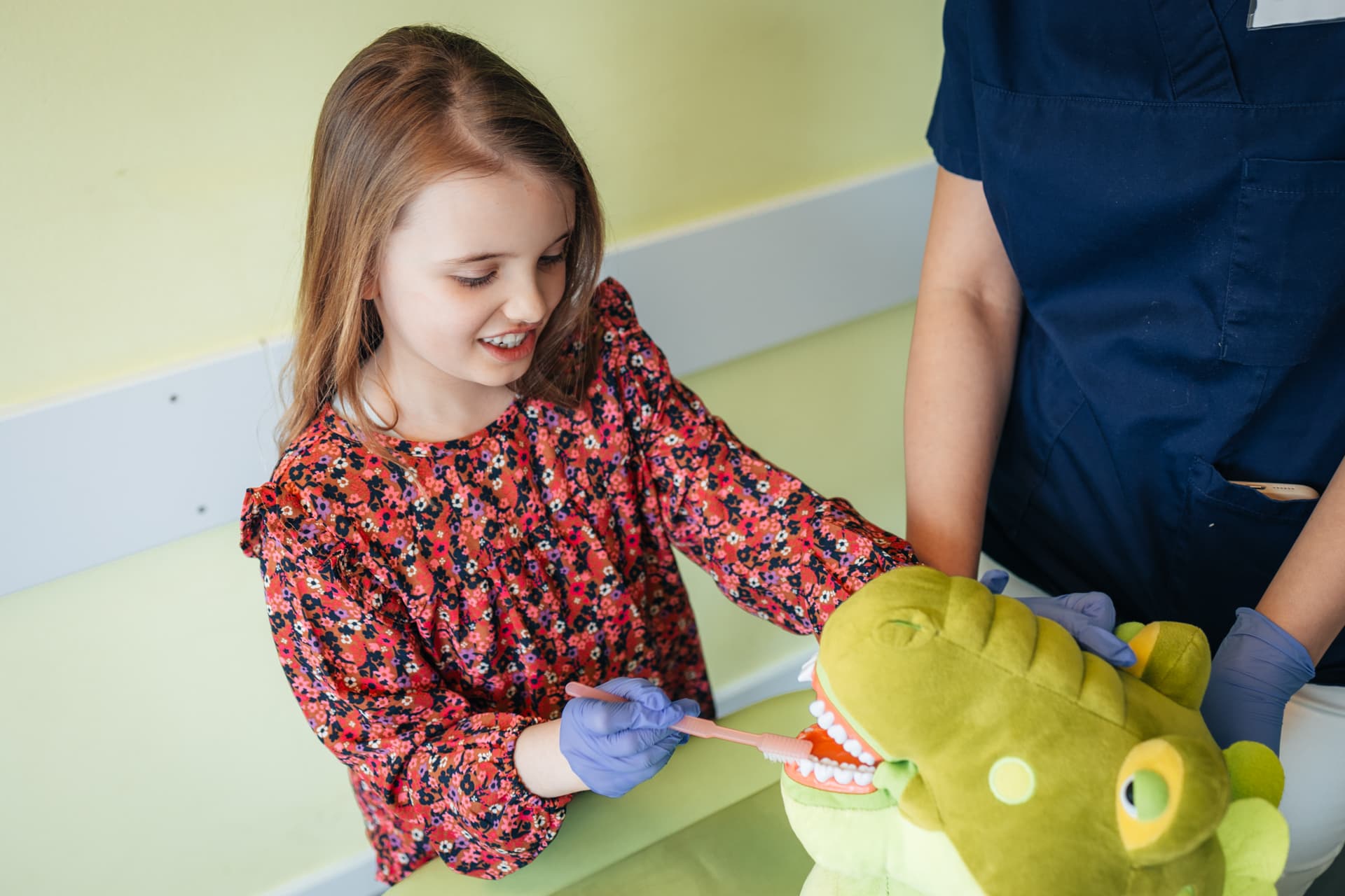 Kinderzahnärztin zeigt spielerisch einem Kind wie man sich richtig die Zähne putzt, mit hilfe einer Zahnatrappe